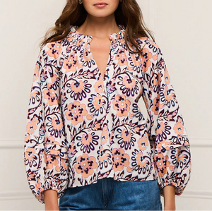 A woman wears the Figue Donna Top, a long-sleeve blouse with a pink, navy, and white floral print, V-neckline, and blouson sleeves for a relaxed fit, paired with blue jeans.