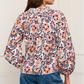 A woman is shown from the back wearing the Figue Donna Top, a long-sleeve blouse with a peach, purple, and white floral print and blouson sleeves, paired with blue jeans.
