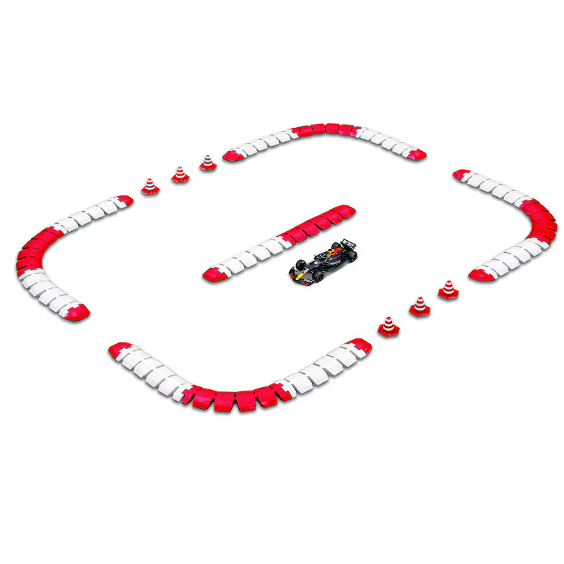 The Maisto R/C 1:41 DC Oracle Red Bull RB2 miniature race car speeds around a small 2.4GHz R/C track featuring red and white barriers and orange traffic cones in a rectangular layout.