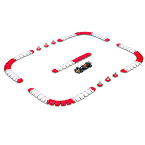 The Maisto R/C 1:41 DC Oracle Red Bull RB2 miniature race car speeds around a small 2.4GHz R/C track featuring red and white barriers and orange traffic cones in a rectangular layout.