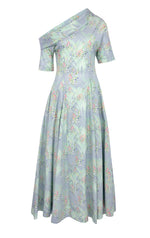 The Bowers Lily of the Valley Dress by Bernadette is a light blue, ankle-length piece with a floral pattern, featuring an asymmetrical off-the-shoulder neckline and short sleeves.