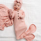 Lou Lou & Company’s Baby Girls’ Piper Plush Knit Knotted Gown features a soft pink design with a matching headband, shown here on a white quilted blanket with a pink blanket nearby—perfect for hassle-free diaper changes.