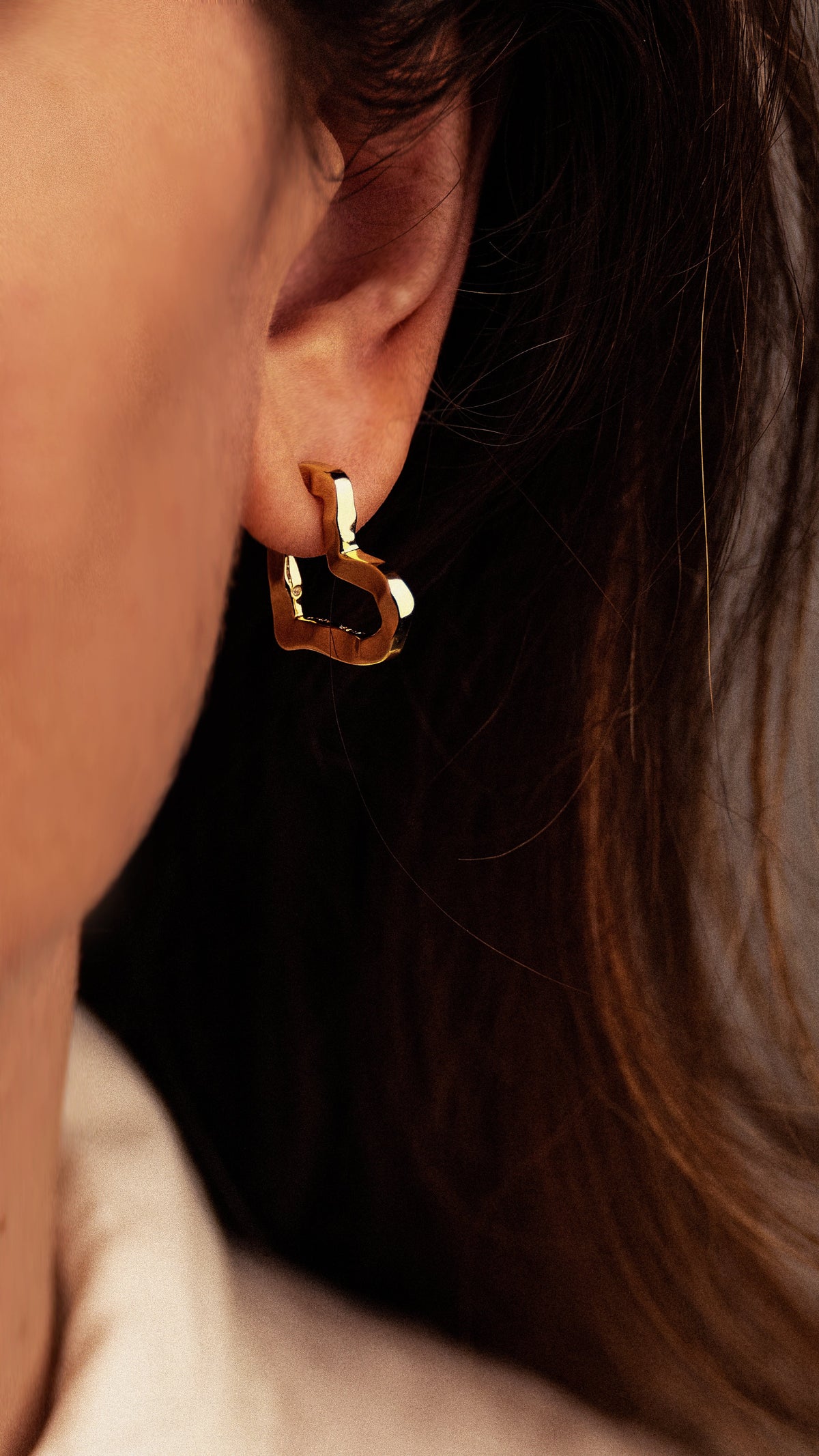 A sculptural 18K gold-plated Small Heart Hoop Earrings piece worn in an earlobe.