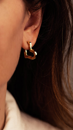 A sculptural 18K gold-plated Small Heart Hoop Earrings piece worn in an earlobe.
