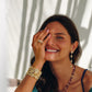 A smiling woman wears Anabel Aram Milos Soleil Drop Earrings, featuring a sunburst motif in 18K gold plated metal.