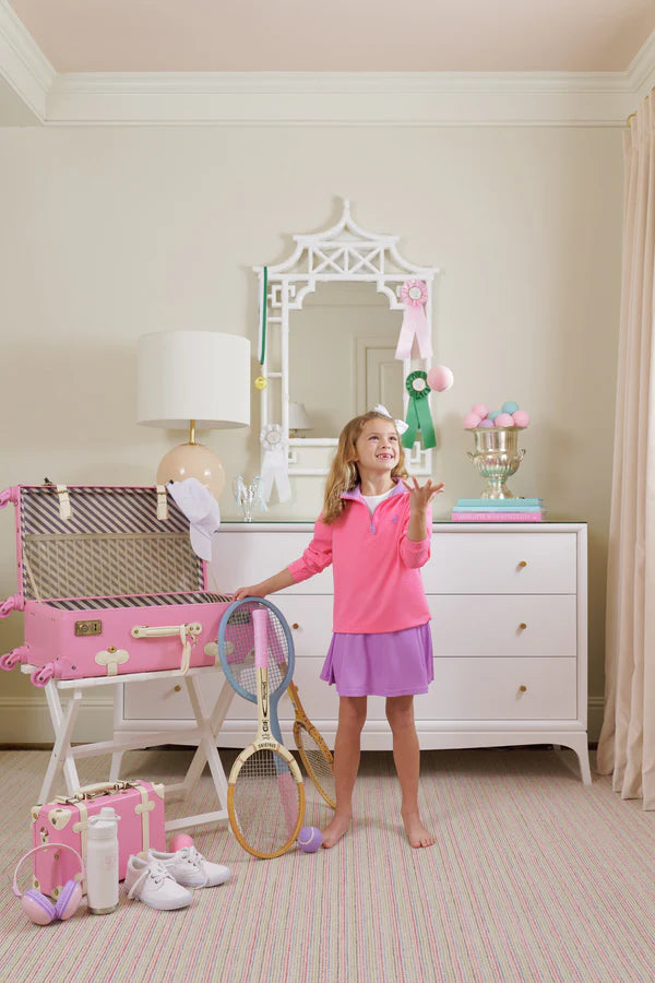 A young girl stands barefoot in a bedroom, tossing tennis balls, wearing The Beaufort Bonnet Company’s Girls' Prepletic™ Hayword Half Zip, with rackets and tennis accessories scattered around her.