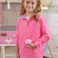 A young girl in The Beaufort Bonnet Company’s Girls' Prepletic™ Hayword Half Zip and a purple skirt holds a tennis ball indoors, with a racket and pink suitcase visible in the background.