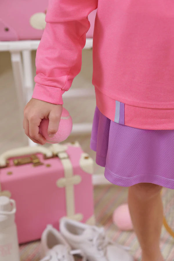 A child in a pink Girls' Prepletic™ Hayword Half Zip by The Beaufort Bonnet Company holds a small pink ball, with a pink suitcase, white shoes, and a white bottle in the background, creating a cozy and playful look.