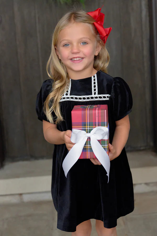 A young girl with blonde hair and a red bow wears The Beaufort Bonnet Company’s Baby Girls' and Girls' Velveteen Dilly Dress while holding a plaid gift box—an adorable pick for holiday wardrobes.