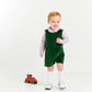 A young child wearing The Beaufort Bonnet Company's Baby Boys' Corduroy Jack Keene Jon Jon stands indoors, holding a string attached to a small red toy train on the floor.