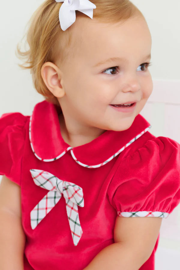 A toddler smiles and looks to the side, wearing The Beaufort Bonnet Company's Baby Girls' Banks Bow Bubble with a matching bow in her hair.