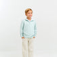 A young boy smiles with hands in pockets, wearing The Beaufort Bonnet Company Baby Boys' and Boys' Hayword Half-Zip in light blue over a white collared shirt, beige pants, and brown loafers against a plain white background.