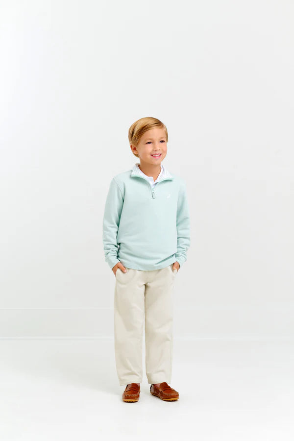 A young boy smiles with hands in pockets, wearing The Beaufort Bonnet Company Baby Boys' and Boys' Hayword Half-Zip in light blue over a white collared shirt, beige pants, and brown loafers against a plain white background.