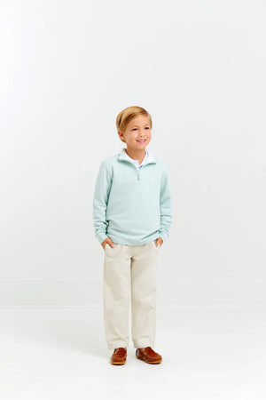 A young boy smiles with hands in pockets, wearing The Beaufort Bonnet Company Baby Boys' and Boys' Hayword Half-Zip in light blue over a white collared shirt, beige pants, and brown loafers against a plain white background.