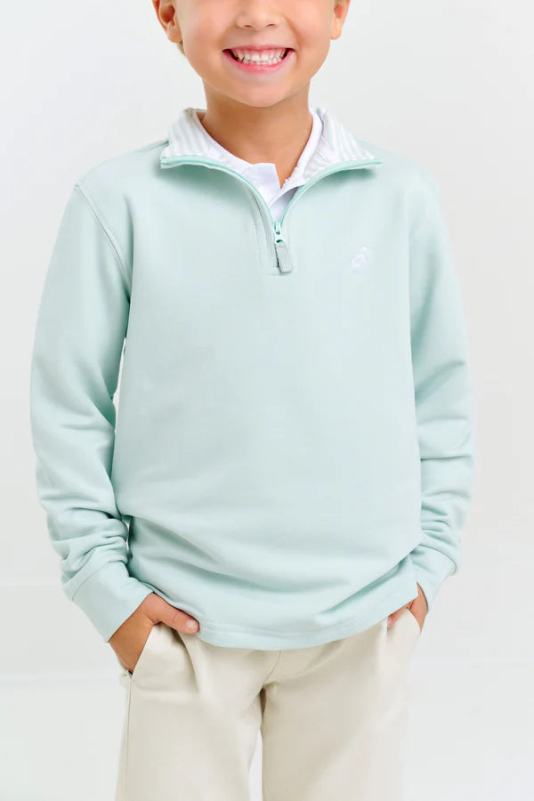 A child smiles with hands in pockets, wearing a light blue Baby Boys' and Boys' Hayword Half-Zip by The Beaufort Bonnet Company and beige pants, standing against a plain background.