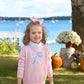 A young girl wears The Beaufort Bonnet Company's Baby Girls' and Girls' Isabelle's Intarsia Sweater while standing outdoors near pumpkins and flowers, with a lake and boats in the background.