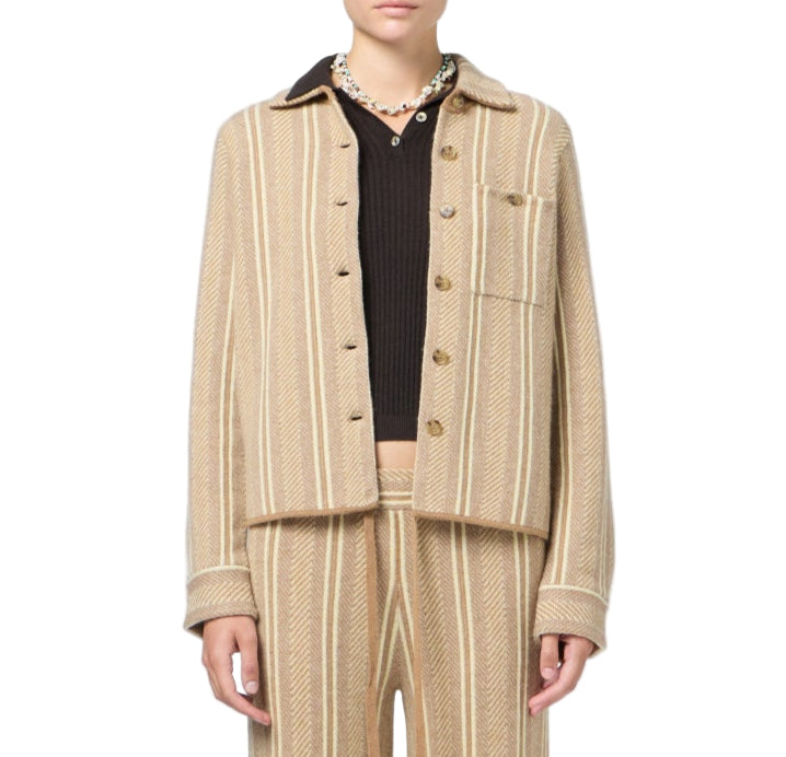A person wearing the Dylan Stripe Shirt by Guest in Residence, featuring beige and cream stripes, paired with matching pants over a black ribbed top and a beaded necklace, shown from shoulders to thighs.