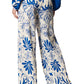 A person is seen from behind wearing the Figue Devon Floral Pant, which showcases an elastic waistband and wide-legged design in a blue and white floral pattern.