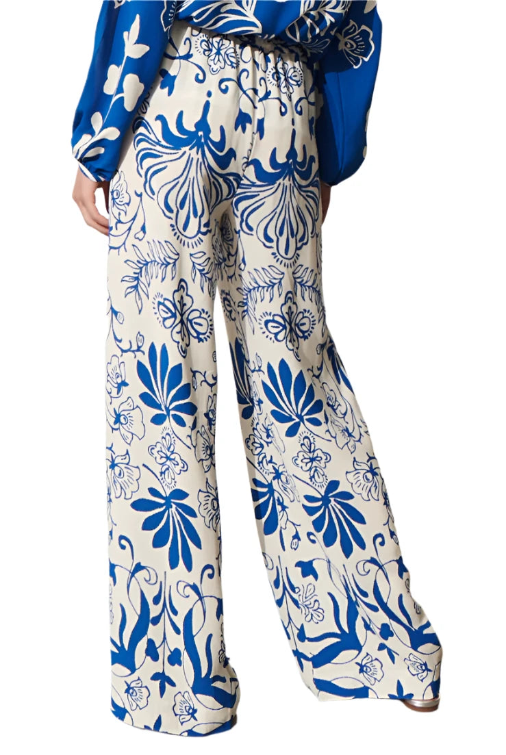 A person is seen from behind wearing the Figue Devon Floral Pant, which showcases an elastic waistband and wide-legged design in a blue and white floral pattern.