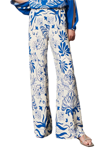 The person is elegantly dressed in the Figue Devon Floral Pant, featuring a blue and white floral pattern with a signature straight silhouette and convenient elastic waistband, paired with a matching blue top.