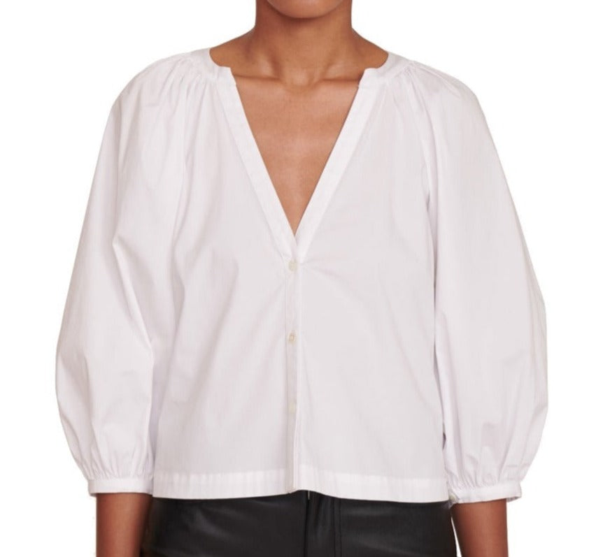 The model is wearing a white Staud Dill Top with a v-neck and leather pants.