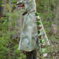 A child wearing the Great Pretenders Grandasaurus T-Rex Cape with Claws stands proudly on a tree stump in a forested area, embodying the spirit of Halloween.