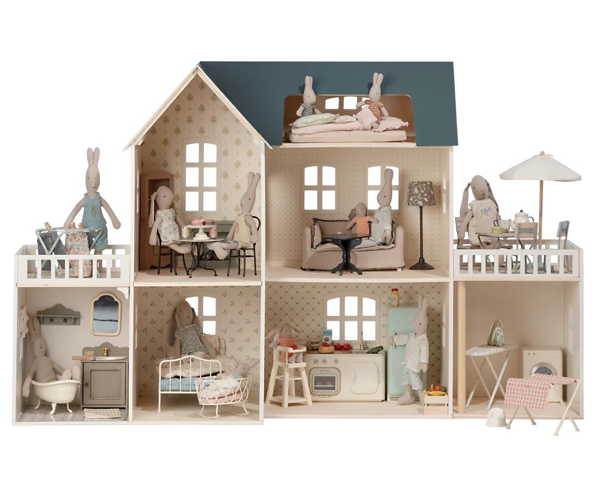 The delightful Maileg Dollhouse, House of Miniature with Wallpaper, is fully furnished with Maileg's exquisite miniature furniture and decor. It features charming rabbit dolls in various rooms, engaging in activities such as cooking, reading, and sleeping.