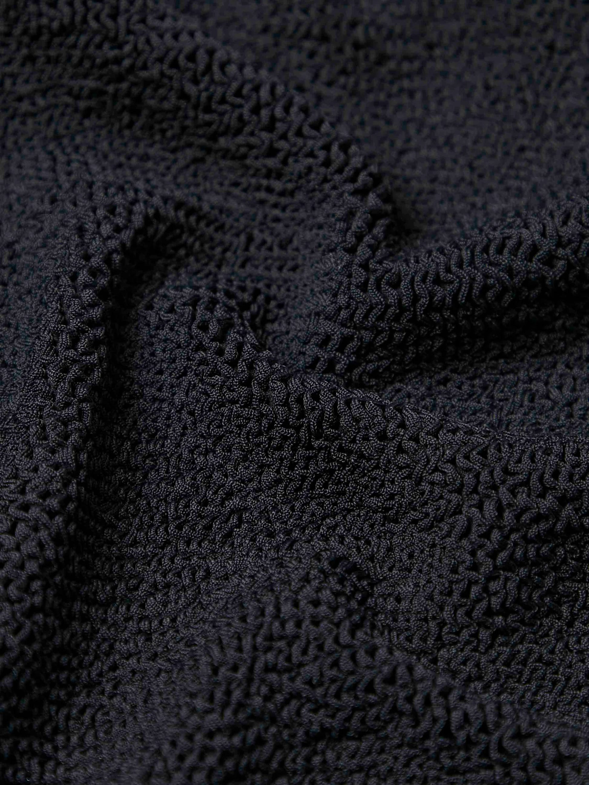 Close-up view of black crinkle fabric with visible ridges and folds, as featured on Hunza G’s Domino Swim one-size swimsuit.