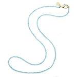 Introducing the Jane Win Double Wrap Beaded Necklace: a delicate, double-strand necklace featuring small light blue beads, finished with a gold clasp and a round gold tag, beautifully displayed on a white background.