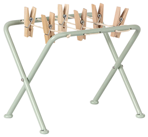 The Maileg Drying Rack with Pegs, Miniature by Maileg is a small, light green foldable rack perfect for handling your laundry routine. Ideal for drying everything from delicate teddies and bunnies to everyday garments, this practical and charming rack features multiple wooden clothespins attached to it.