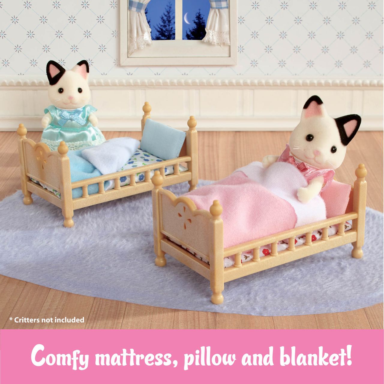 Two Calico Critters cat figures rest in the Stack and Play Beds by Calico Critters, complete with comfy mattresses, pillows, and blankets. The cozy dollhouse bedroom features a window and a blue rug. Text at the bottom says, “Comfy mattress, pillow and blanket!”.