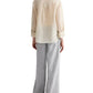 A person stands with their back to the camera, wearing TWP’s Boyfriend Silk Top in beige stripes and loose-fitting light gray pants, set against a white background.