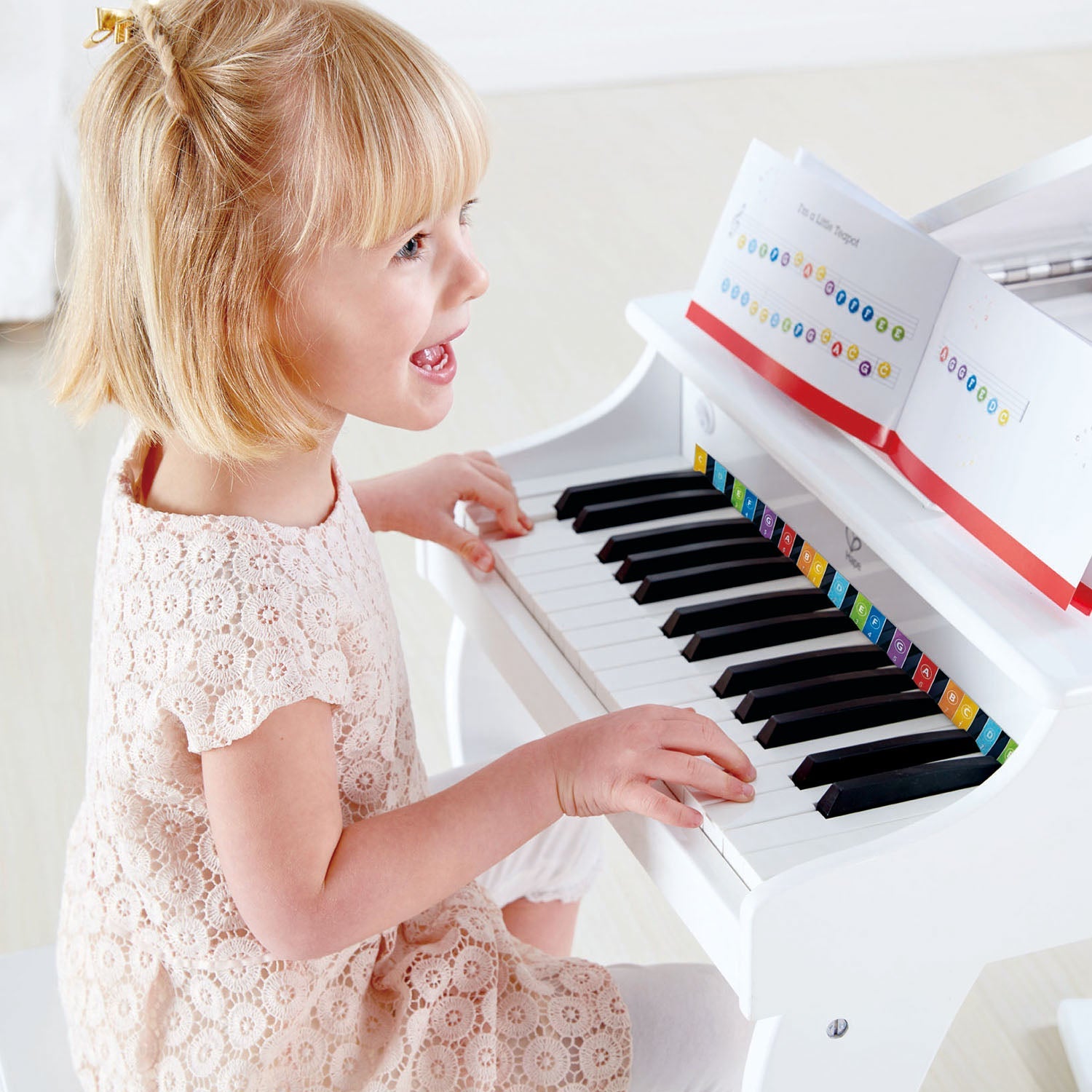 A young child playing a 30-key Hape Deluxe White Grand Piano with color-coded keys.