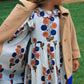 Young girl stands on grass, wearing a tan coat over the Pink Chicken Girls' Darcy Dress with blue and orange patterns, looking to the side.