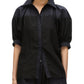 A person wearing the 3.1 Phillip Lim Lantern Sleeve Combo Shirt, a black short-sleeve button-up with a collar, exuding feminine elegance through its structured silhouette.