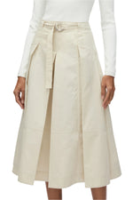 A person wearing the 3.1 Phillip Lim Utility Pleated Skirt with a belt in beige, paired with a long-sleeved white top.