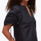 A woman wears the 3.1 Phillip Lim Ruched Sleeve V-Neck Top, a dark short-sleeve blouse in technical poplin with ruched sleeves and a V-neck—combining elegance with modern style. Shown from the chest up.