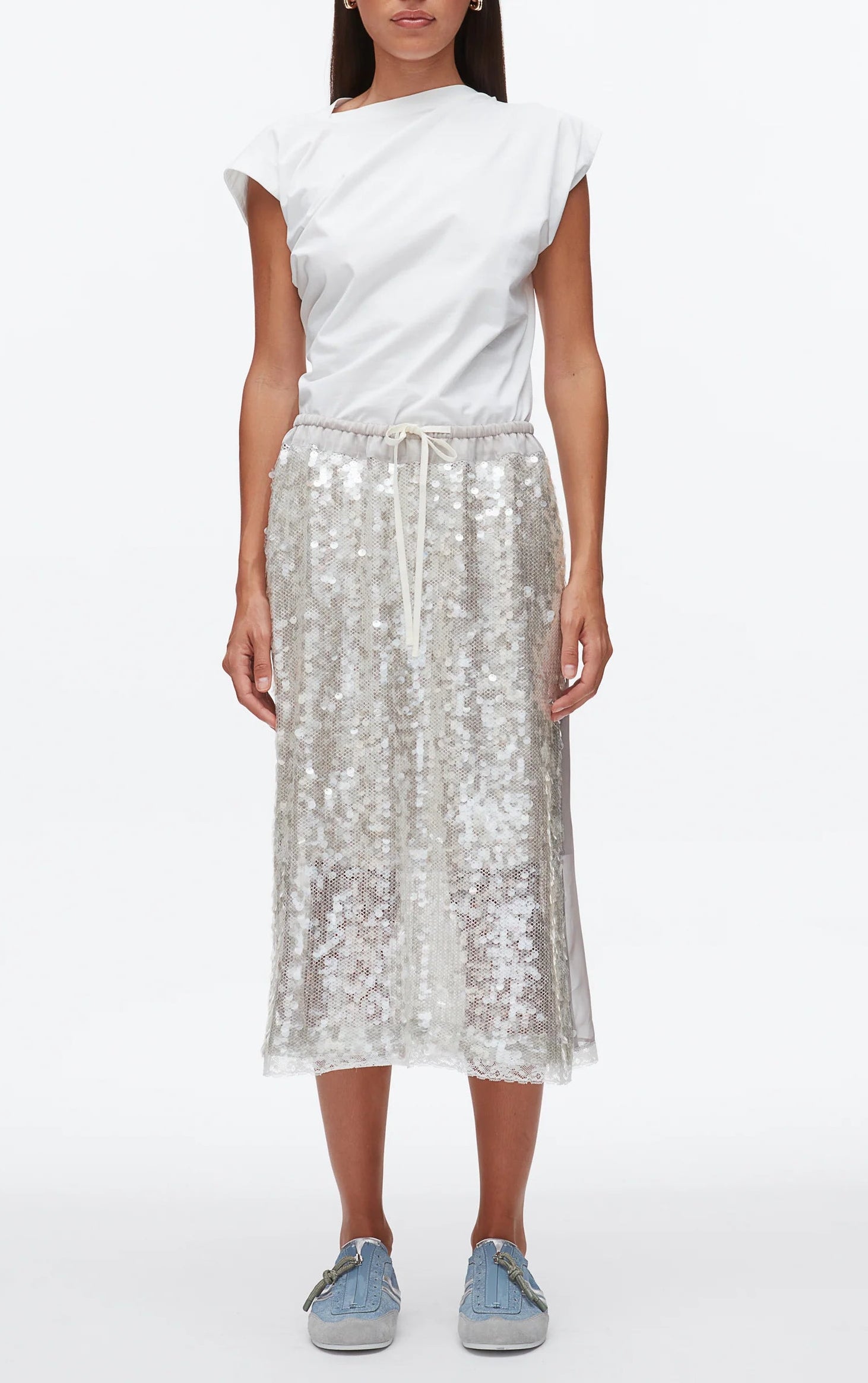 A woman faces forward wearing a white short-sleeve top, light blue sneakers, and the 3.1 Phillip Lim Sequin Pull On Skirt—a silver sequin midi skirt with a drawstring waistband.