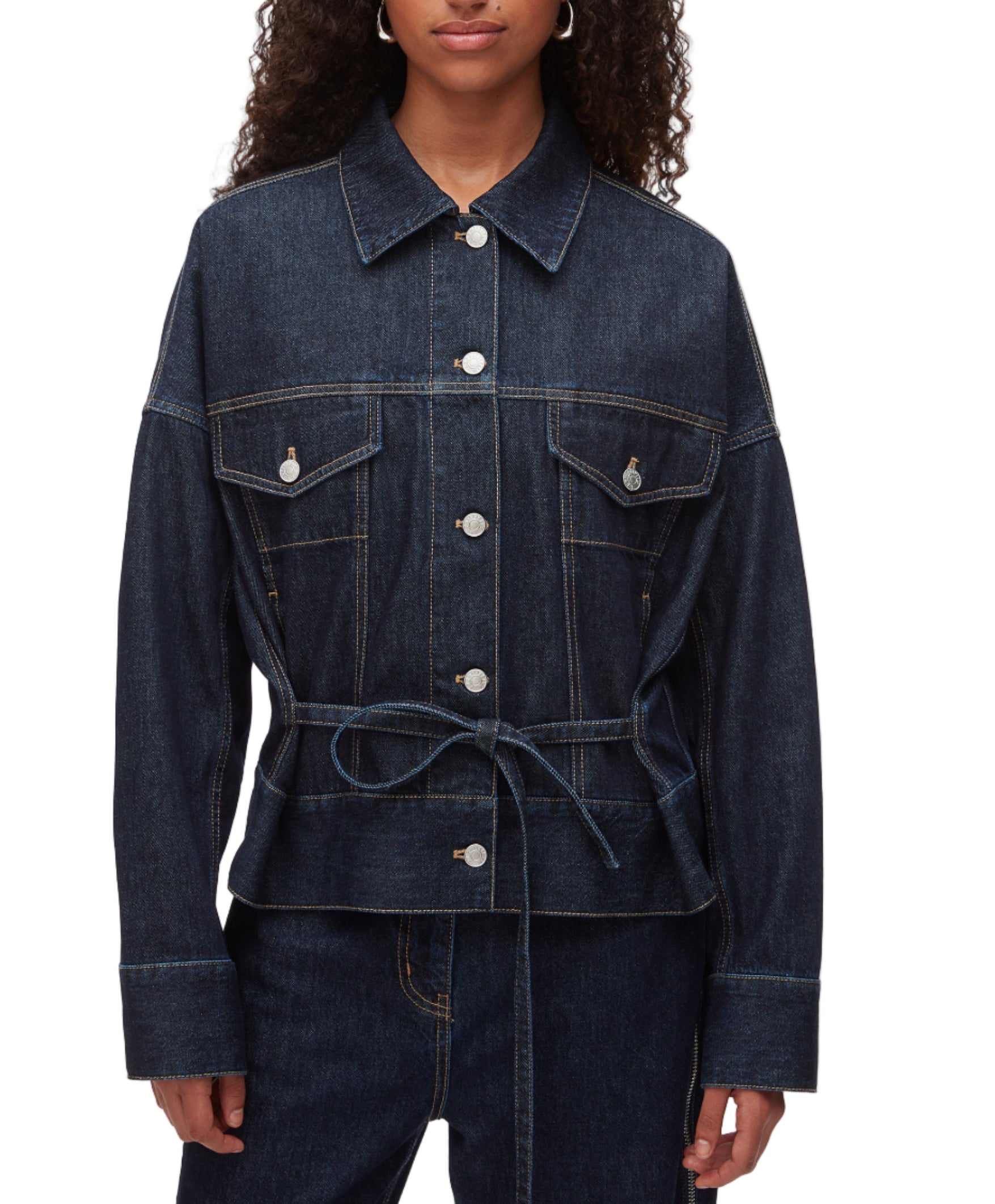 A person wears the 3.1 Phillip Lim Denim Boxy Jacket, featuring front pockets, button closure, and a waist tie, styled with matching denim pants for a coordinated look.