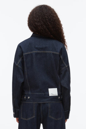 A person with long curly hair wears the 3.1 Phillip Lim Denim Boxy Jacket, photographed from the back against a plain background.