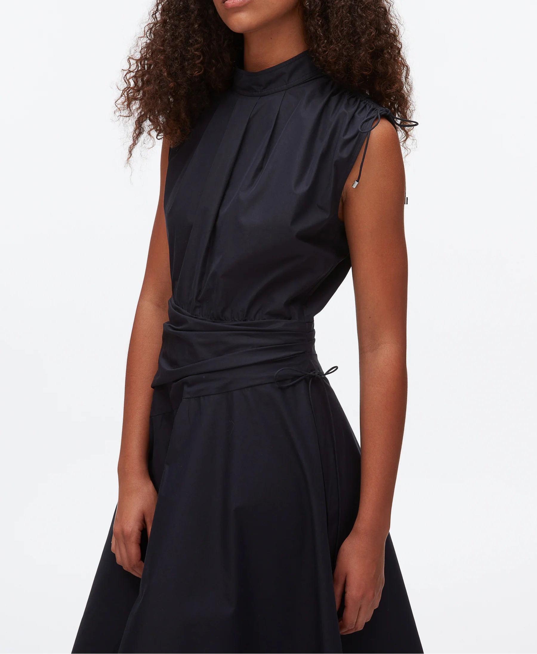 A woman models the 3.1 Phillip Lim Ruched Handkerchief Dress—a sleeveless, high-neck black dress with a fitted waist and subtle gathers—in crisp technical poplin, standing against a plain white background.
