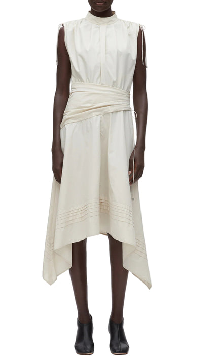 A person wears the 3.1 Phillip Lim Ruched Handkerchief Dress, an off-white sleeveless midi in technical poplin with a wrap waist and handkerchief hem, paired with black ankle boots.
