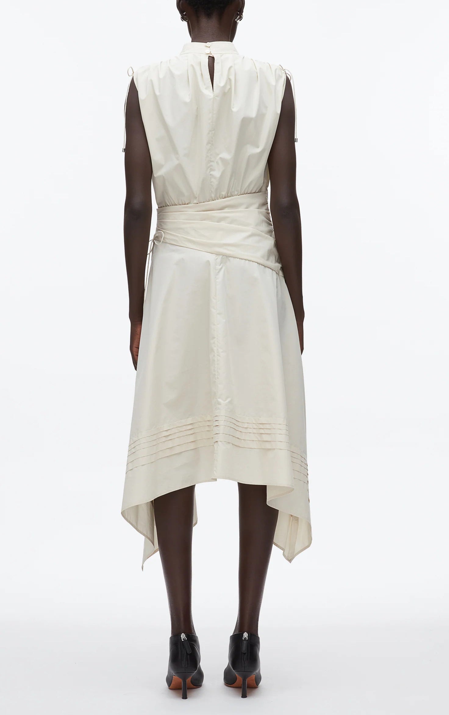 A person faces away in a 3.1 Phillip Lim Ruched Handkerchief Dress made from technical poplin with an off-white handkerchief hem, paired with black heeled shoes, set against a plain white background.
