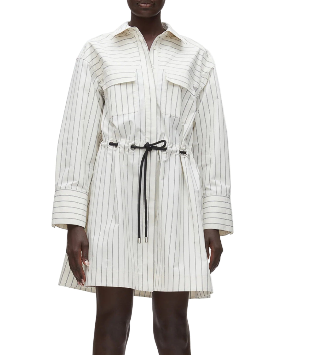 A person wears the 3.1 Phillip Lim Belted Mini Shirt Dress, a white long-sleeve shirtdress with thin black vertical stripes, front pockets, a collar, and a black drawstring waist.