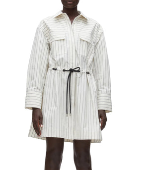 A person wears the 3.1 Phillip Lim Belted Mini Shirt Dress, a white long-sleeve shirtdress with thin black vertical stripes, front pockets, a collar, and a black drawstring waist.