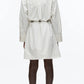 A person stands with their back to the camera, wearing the 3.1 Phillip Lim Belted Mini Shirt Dress—a long-sleeve, striped poplin dress—paired with white heeled shoes.