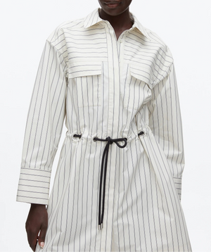 A person wears the 3.1 Phillip Lim Belted Mini Shirt Dress, designed with long sleeves, chest pockets, and a black waist belt for a modern look.