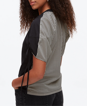 A woman wears the 3.1 Phillip Lim Ruched T-Shirt with Combo Panel Back—featuring black fabric on one side and black-and-white vertical stripes on the other—paired with black jeans.