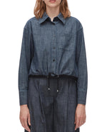 A person models the 3.1 Phillip Lim Denim Cropped Shirt, featuring a drawstring hem, paired with matching denim pants to showcase a modern silhouette against a plain background.