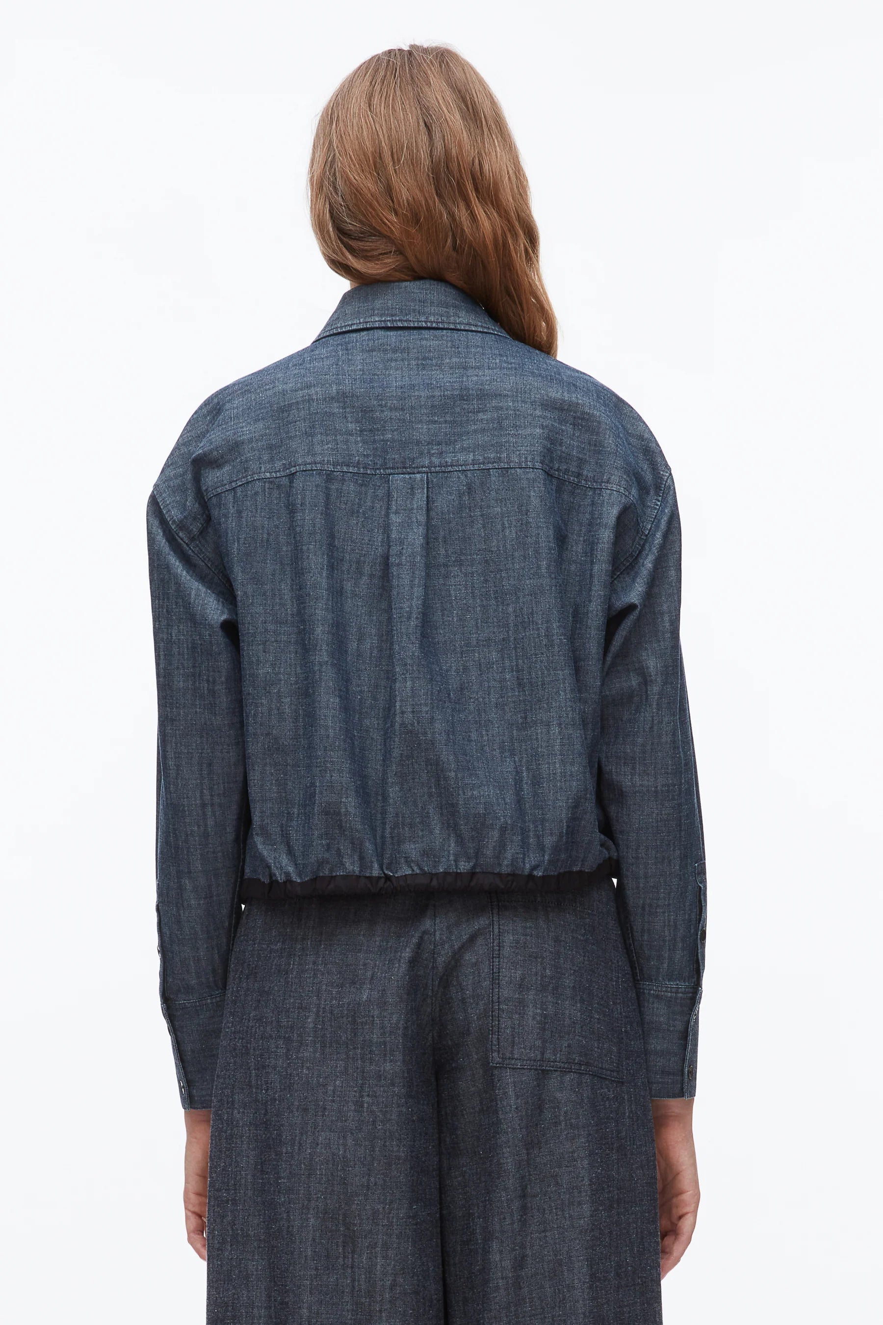 A person with long brown hair models the 3.1 Phillip Lim Denim Cropped Shirt, shown from the back against a plain white background, paired with matching pants for a coordinated look.
